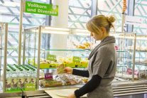 Frau wählt Vollkornbrot mit grünem Smiley an der Essensausgabe